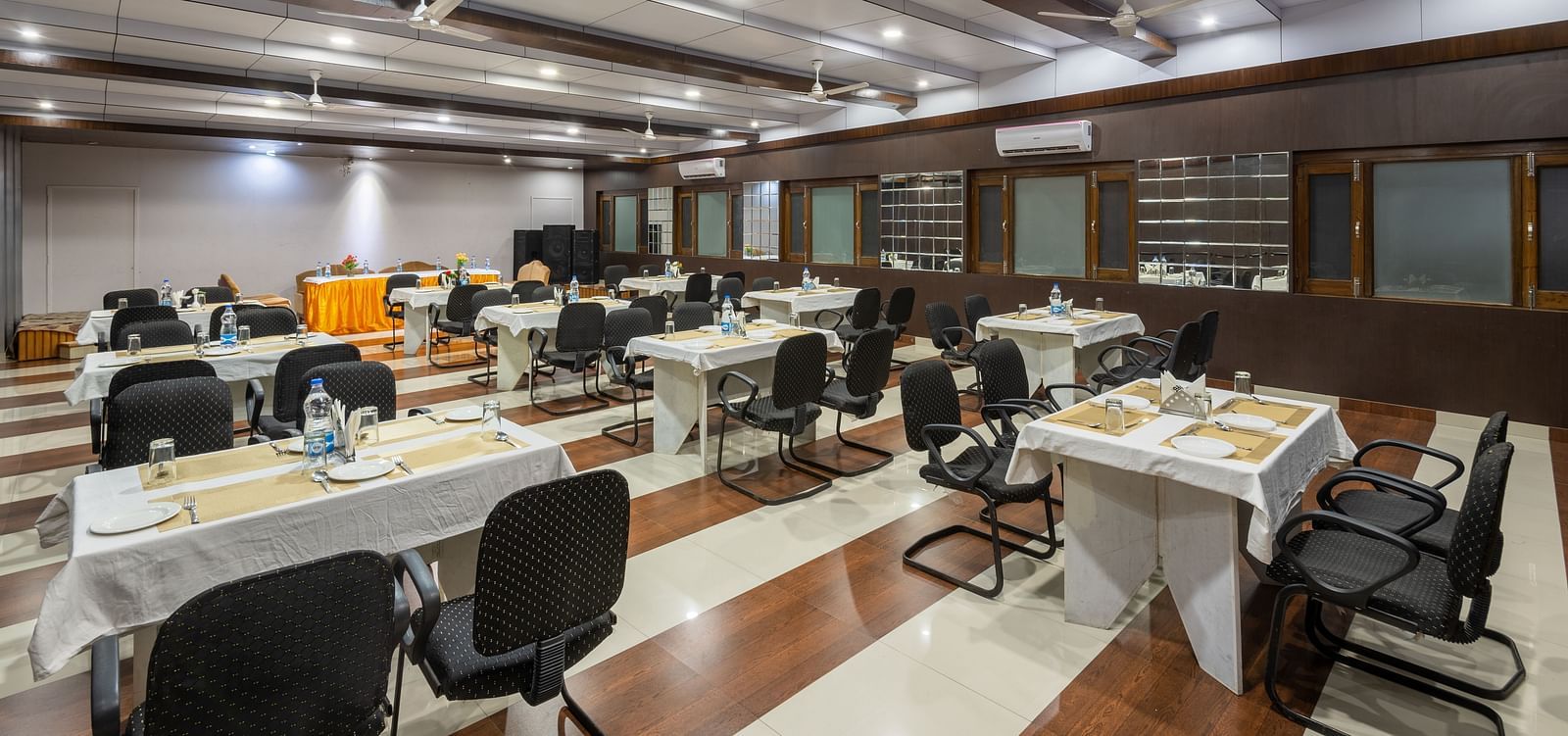 A large, well-lit conference room with rows of tables and chairs arranged for a meeting - DLS Meghavan Resort 